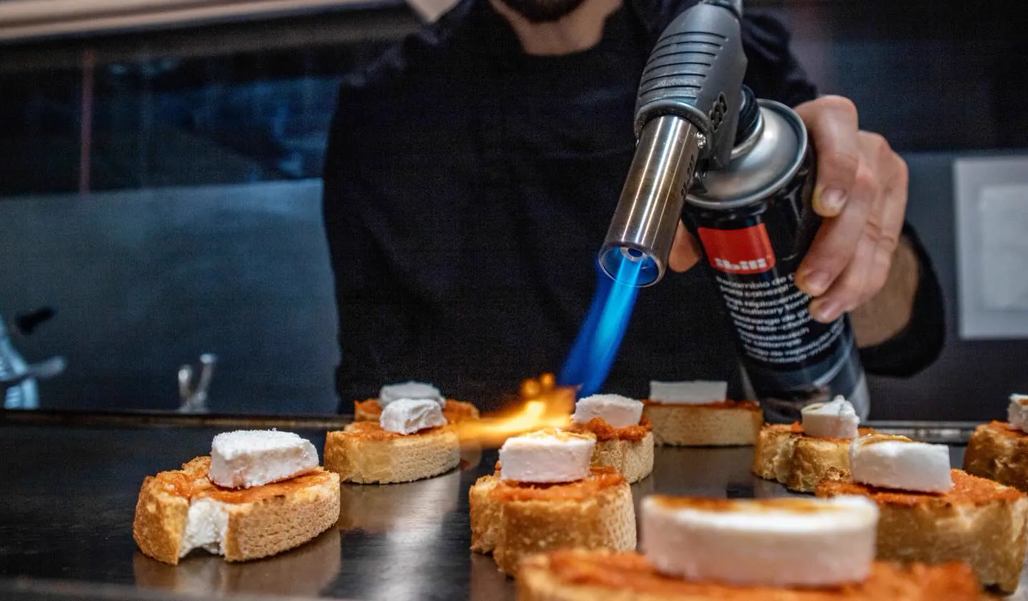 Cocinero gratinando con soplete queso de cabra sobre tostas